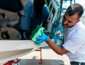 Man in white t-shirt cleaning his boat's hull with a green microfiber cloth in preparation for a boat show