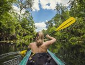 Woman in green kayak paddling down a calm river surrounded by trees in Florida