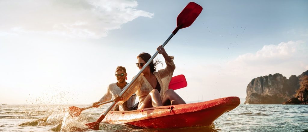 Young couple sharing a red kayak smiling and laughing while paddling through shallow ocean water in New Jersey