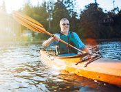 Man in an orange kayak smiling and paddling through the water in the Finger Lakes