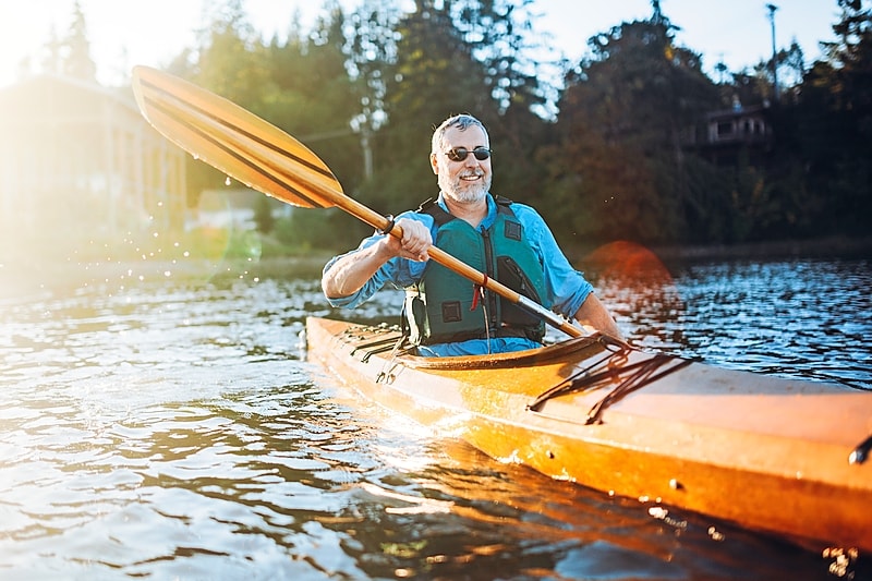 Man in an orange kayak smiling and paddling through the water in the Finger Lakes