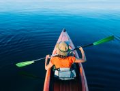 Woman in orange shirt kayaking facing away from camera