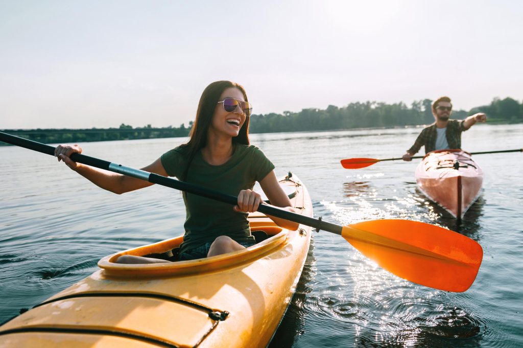 A young couple of kayakers smiling and laughing while paddling through calm water on a sunny day