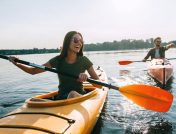 A young couple of kayakers smiling and laughing while paddling through calm water on a sunny day