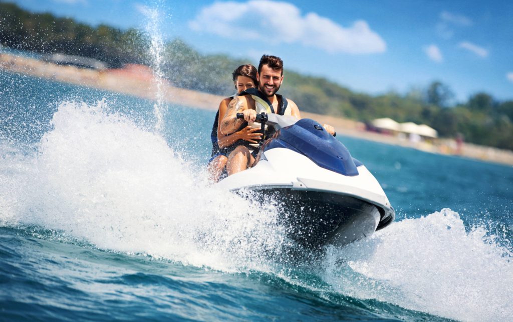 Young couple driving a blue and white jet ski in the ocean next to a beach