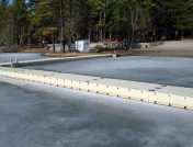 White narrow floating dock by the shoreline surrounded by ice during winter