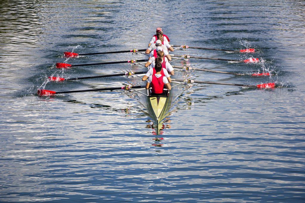 A rowing team of eight people paddling in unison through a calm lake