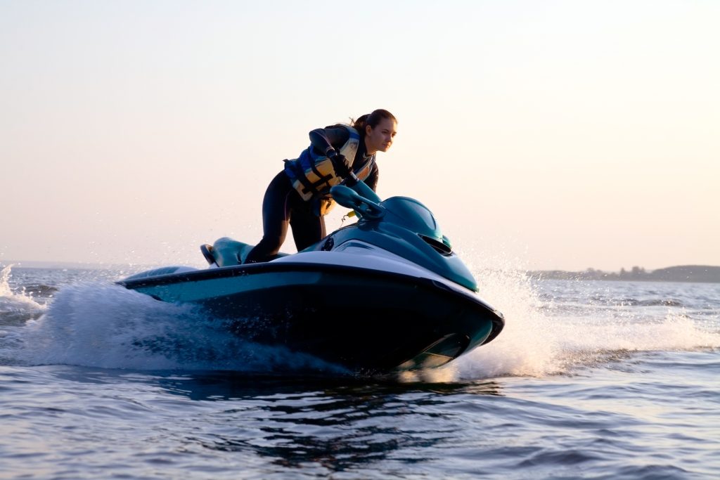 Woman in yellow life vest driving a green and white jet ski at high speeds