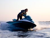 Woman in yellow life vest driving a green and white jet ski at high speeds