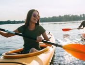 A young couple of kayakers smiling and laughing while paddling through calm water on a sunny day in Michigan