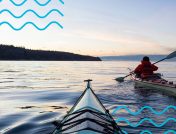 Two kayakers paddling over calm water on a cold winter morning